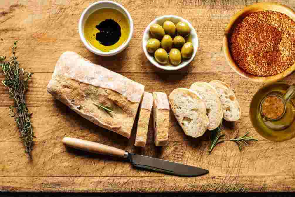 pan con aceite y semillas de lino linaza y aceite de oliva aceitunas sobre tabla de madera y romero