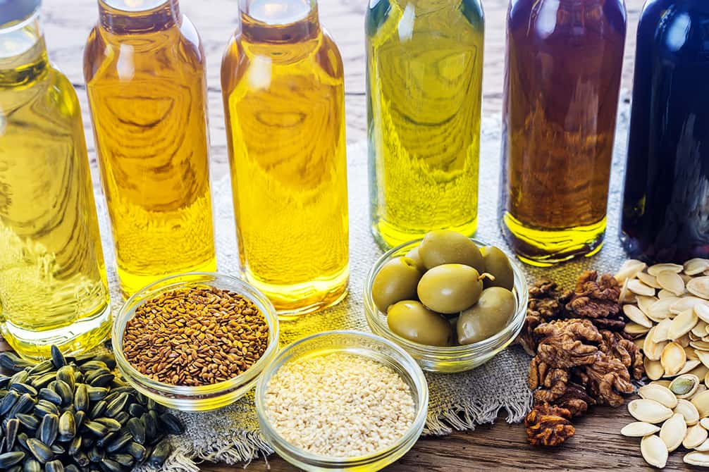 botellas de distintos aceites vegetales aceite de oliva linaza lino girasol calabaza nuez sobre una mesa