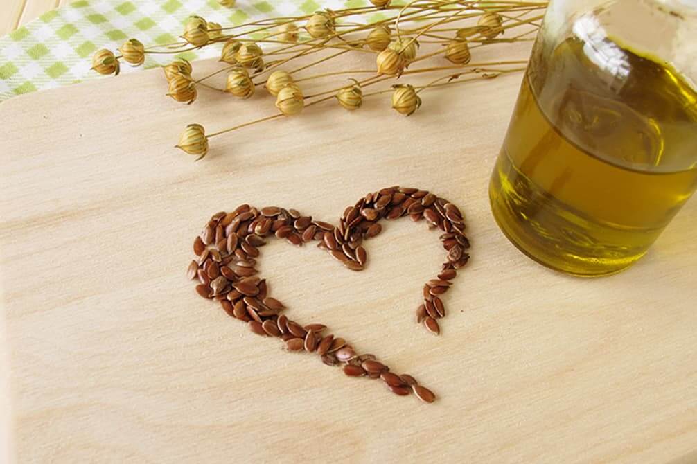 aceite de lino con semillas de lino en forma de corazon y ramas de lino encima de madera