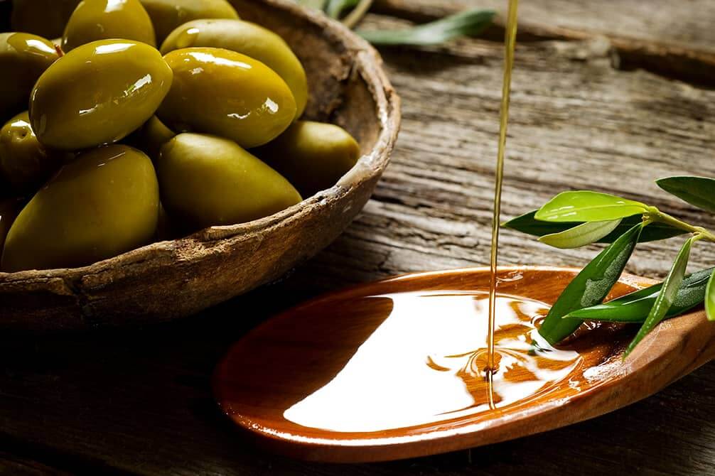 un plato de aceitunas y un chorro de aceite de oliva que cae sobre cuchara de madera