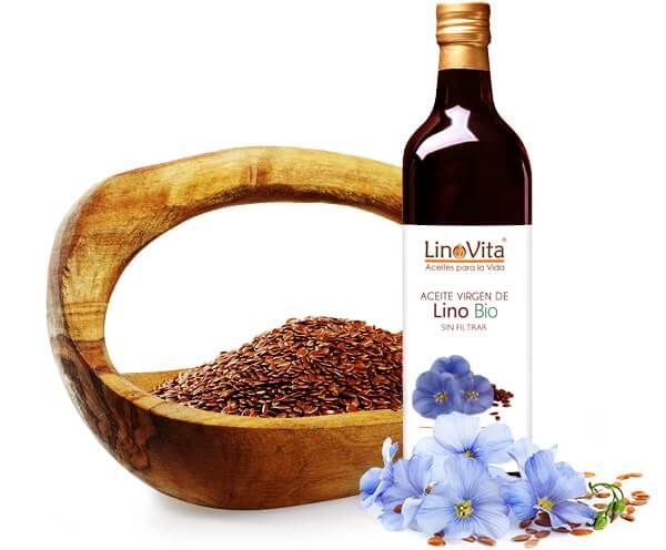 botella de aceite de lino refrigerado con flores de linaza y una cesta de madera con semillas de lino